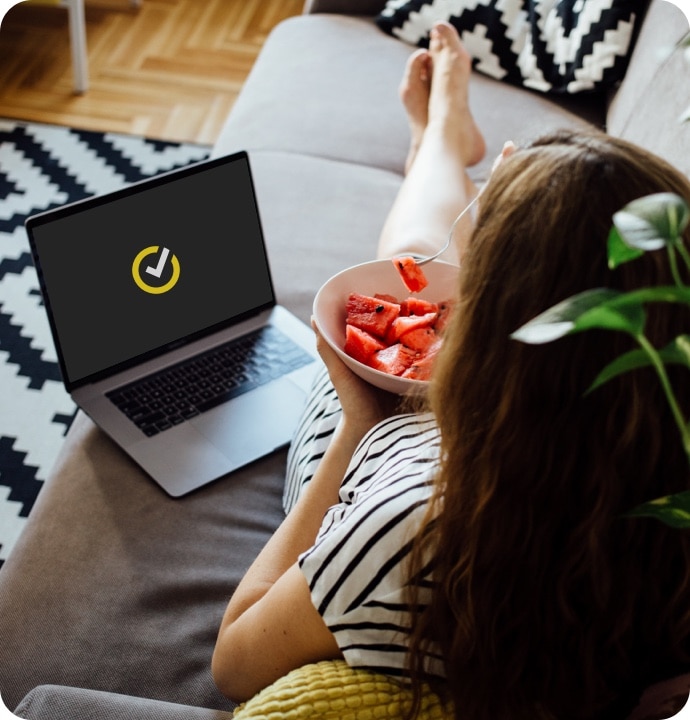 Mujer comiendo sandía en el sofá con un portátil iniciando Norton 360 AntiVirus Plus